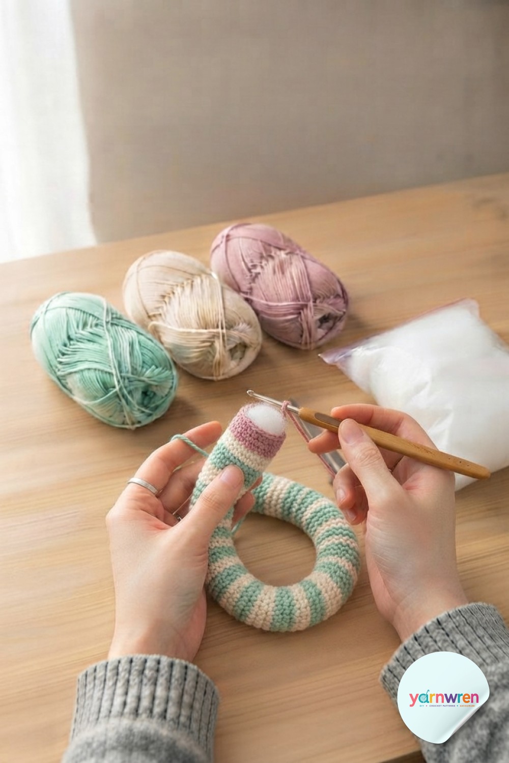 The half-finished striped body of the crochet snake amigurumi pattern coils on the table as a pink round is added.