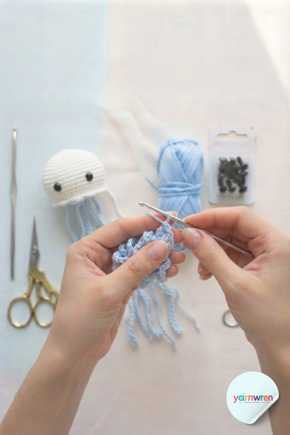 Crocheting light blue tentacle chains beside a finished white head for jellyfish keychain crochet